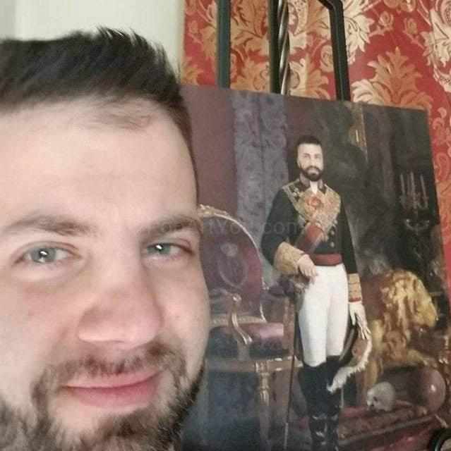 A man stands against the background of a portrait of himself, dressed in regal attire