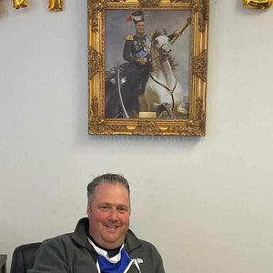 A man sits next to a portrait of himself riding a horse dressed in renaissance regal attire