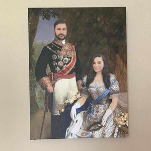 The portrait shows a couple dressed in silver regal attires sitting near a tree hanging on a beige wall