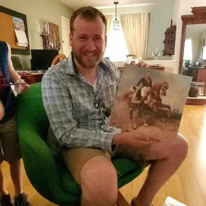 A man holds a portrait of himself sitting on a horse dressed in renaissance regal clothes